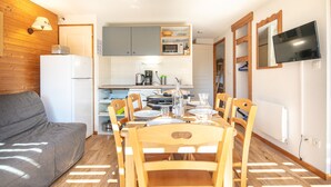 Un espace de vie compact comprenant un coin repas, une kitchenette et un téléviseur fixé au mur.