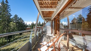 Une terrasse en bois dotée d’une balustrade en verre, qui offre une vue sur une zone boisée.