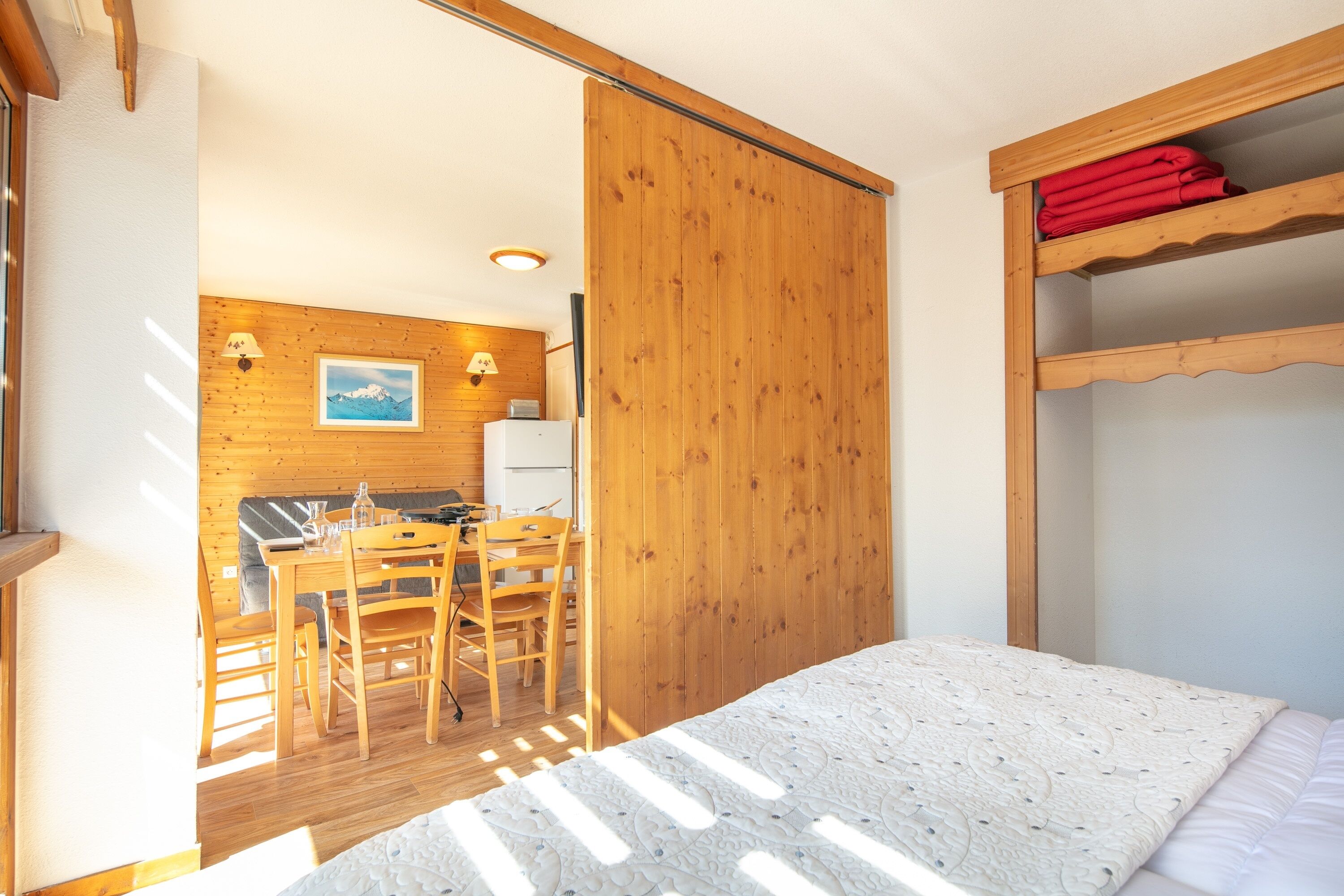 A room with a bed, wooden furniture, a dining area, and a view of a kitchen.