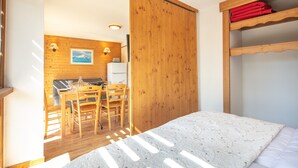 Une pièce comprenant un lit, des meubles en bois, un coin repas et donnant sur une cuisine.