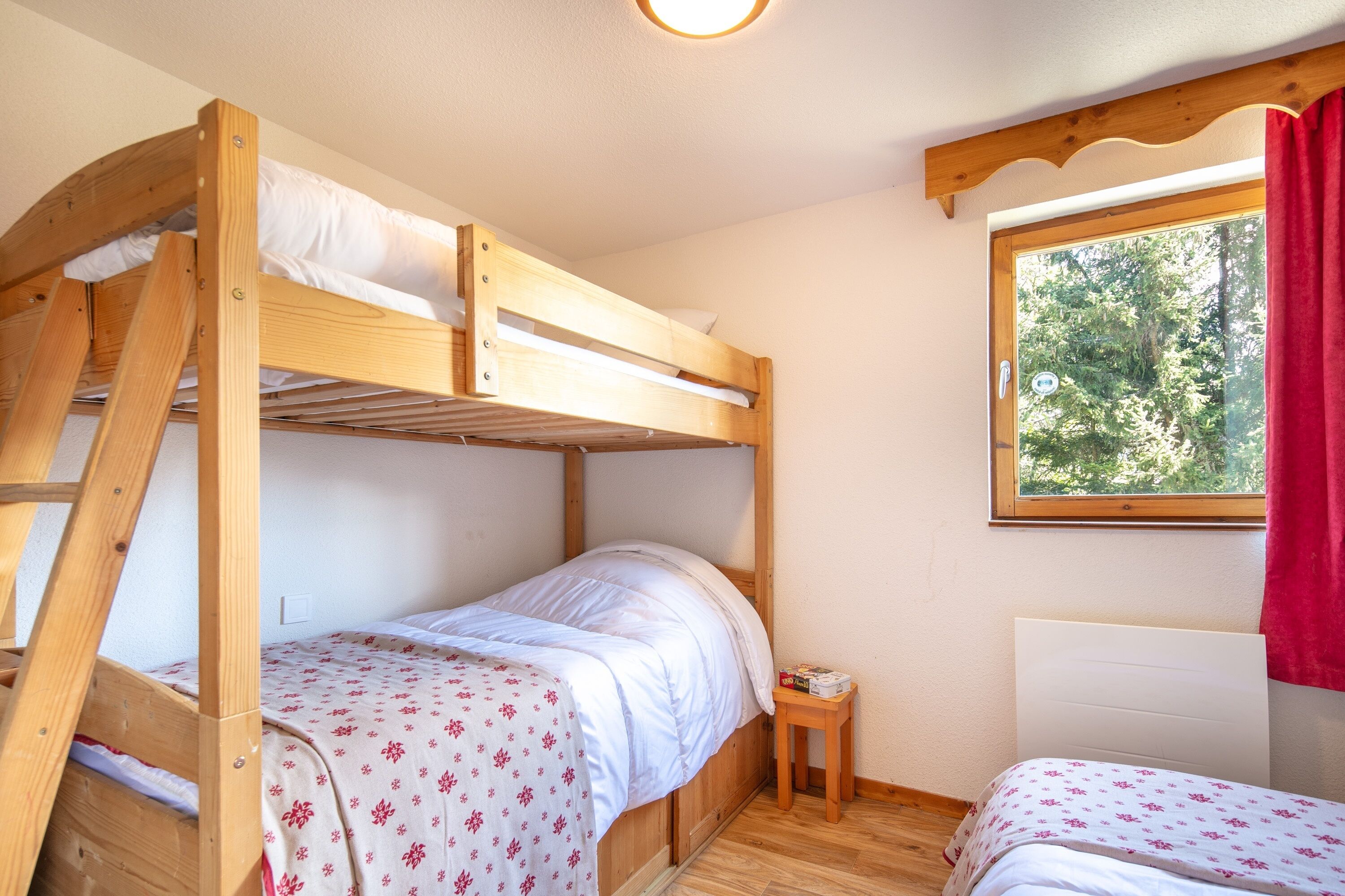 Une chambre avec un lit superposé, une petite table et une fenêtre donnant sur les arbres.