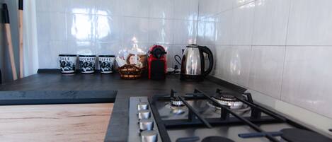 A kitchen with a gas stove, a coffee maker, and several mugs on the counter.