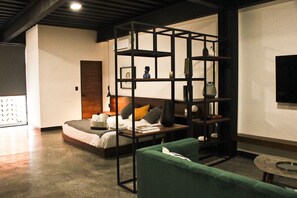 Une chambre d’hôtel moderne avec un lit, un canapé vert, une petite table et une étagère décorative noire.