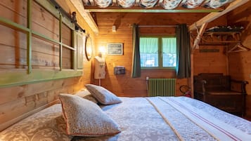 A cozy wooden room with a bed, pillows, a hanging light, a window with curtains, and a radiator.