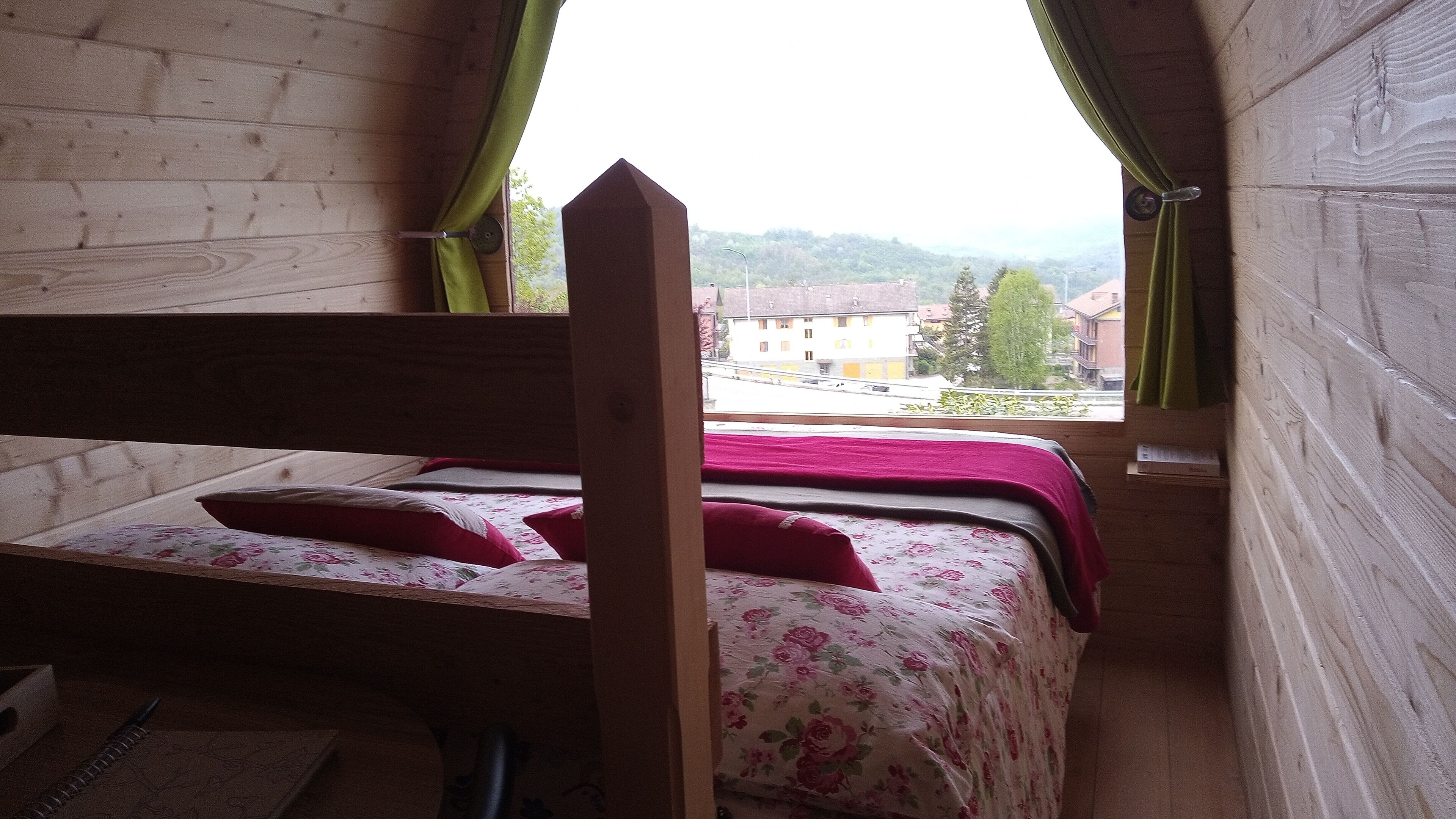 A wooden room with a bed, a window, and a view of buildings.