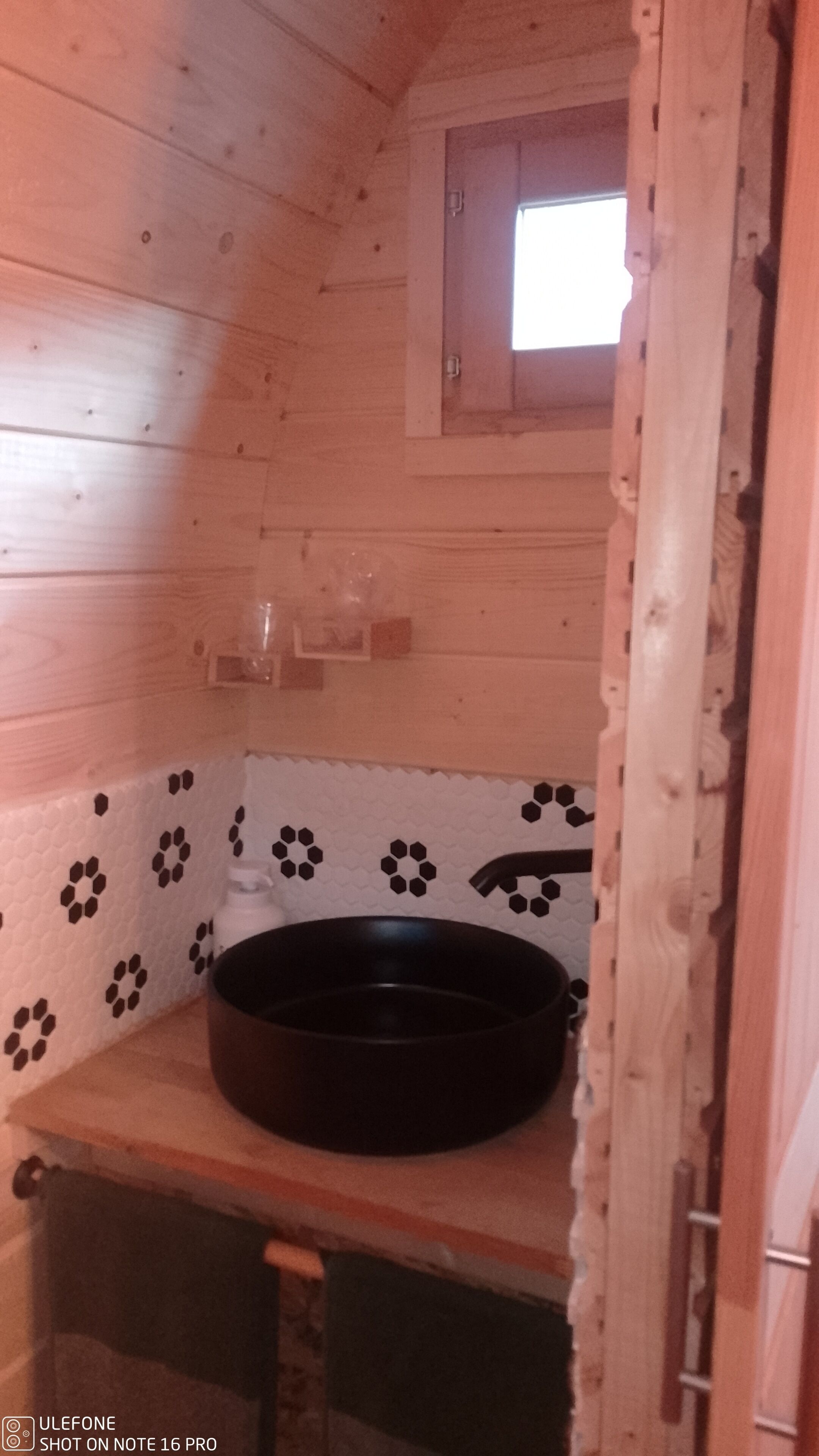 A small, cozy cabin with a wooden interior, a black circular object on a wooden shelf, and a small window.