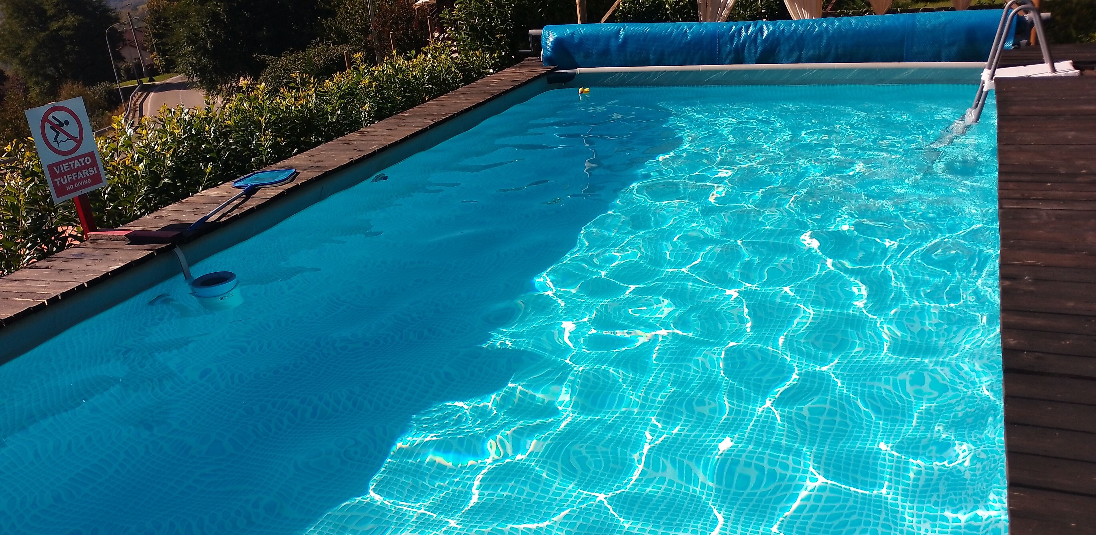 Una piscina con agua azul cristalina, rodeada por una terraza de madera y un cartel que indica prohibido bucear.