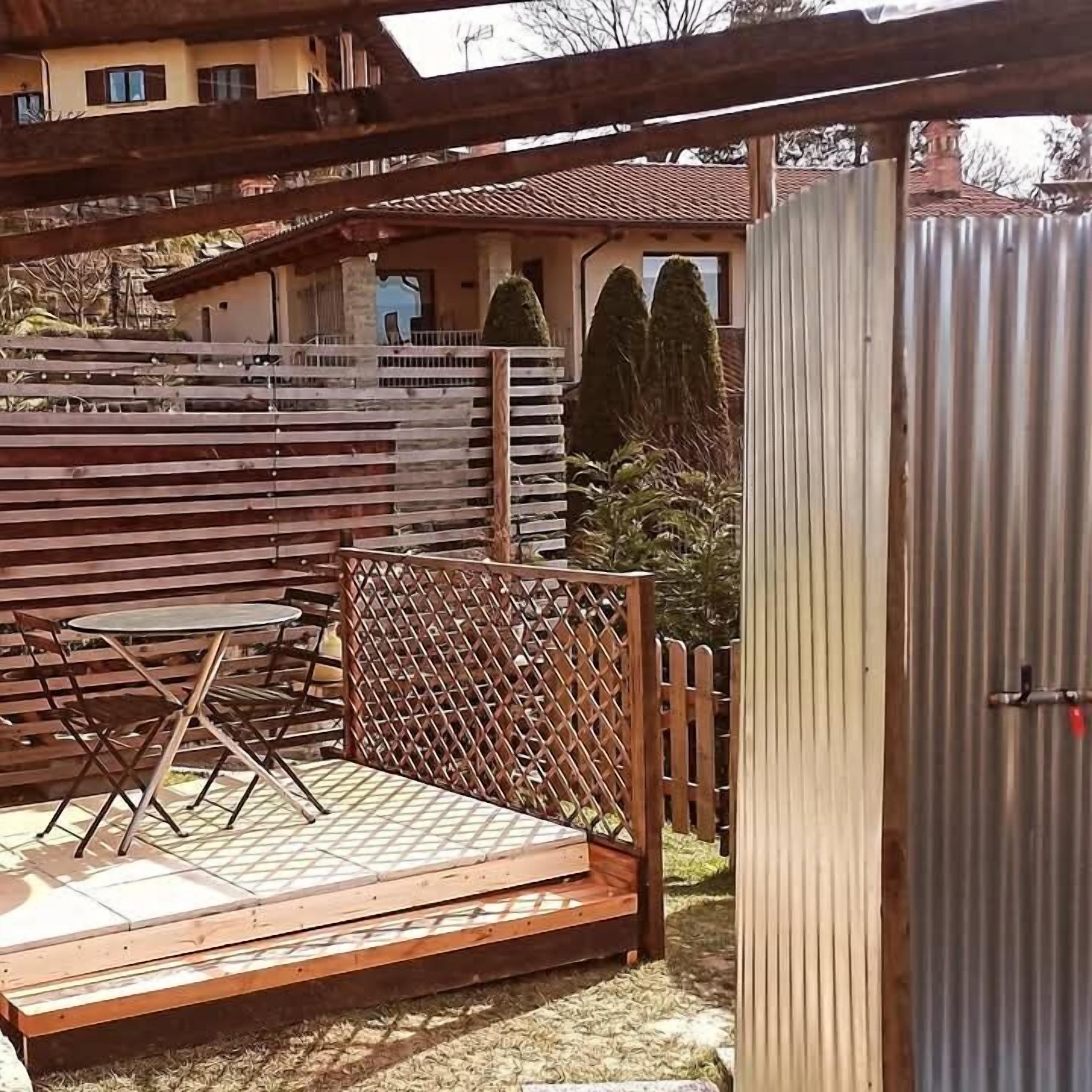 Un patio al aire libre con una mesa y sillas de madera, una valla de metal y una estructura de metal corrugado.