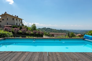 Una piscina con cubierta de madera, rodeada de abundante vegetación y vistas a colinas distantes.