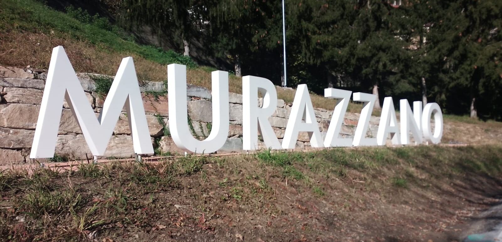A large white sign with the word "MURAZZINO" on a stone wall.