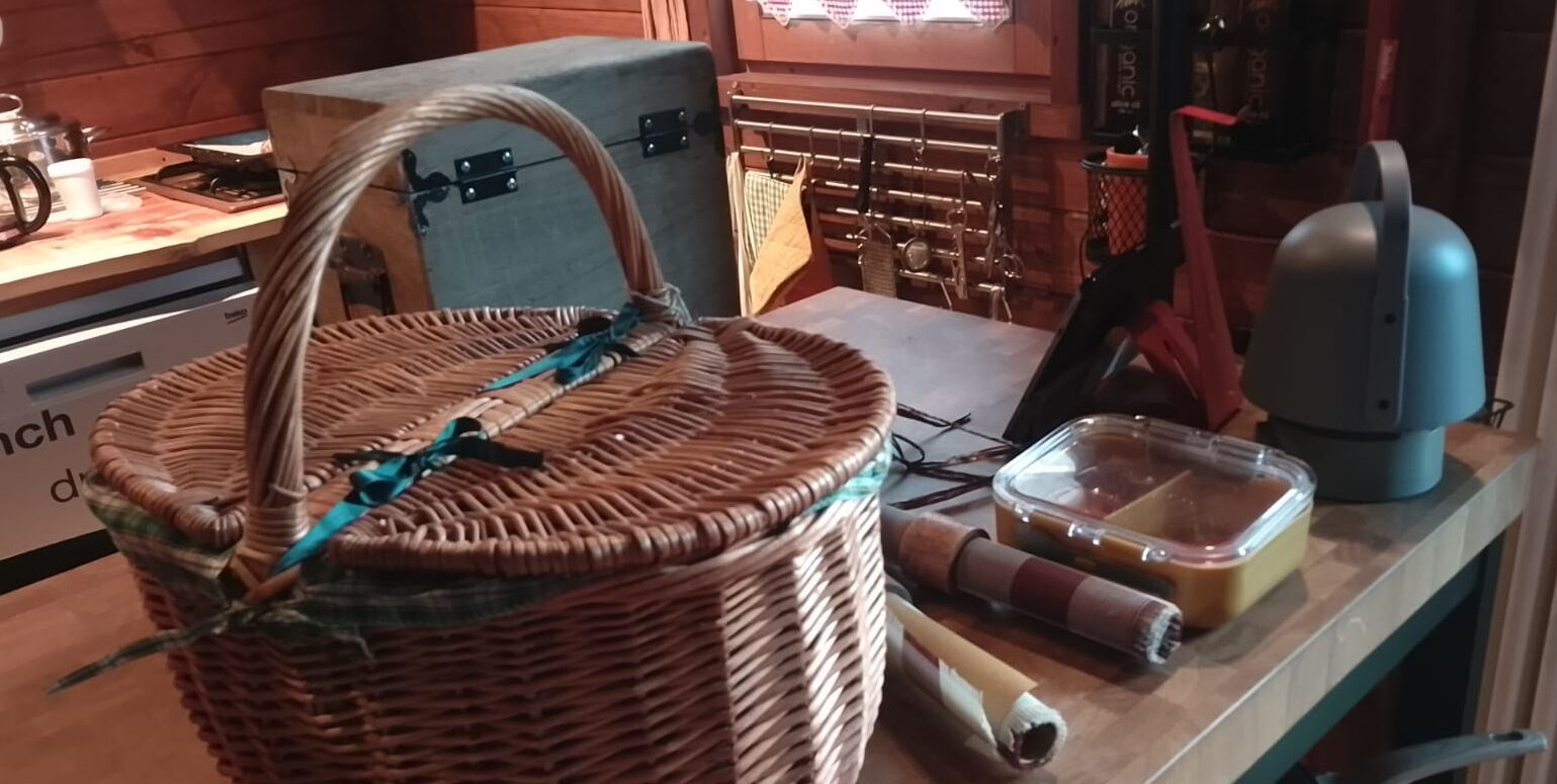 Un panier en osier avec une anse, posé sur une table en bois, un récipient en plastique et un appareil électroménager bleu.