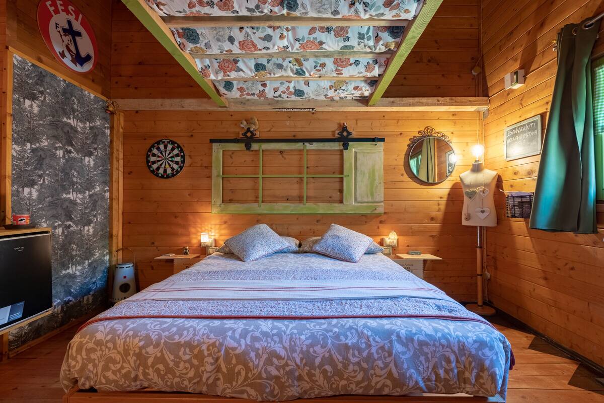 Ein gemütlicher Holzraum mit einem Bett, einer Dartscheibe, einem Spiegel und einer Wand mit einem Blumenmuster.