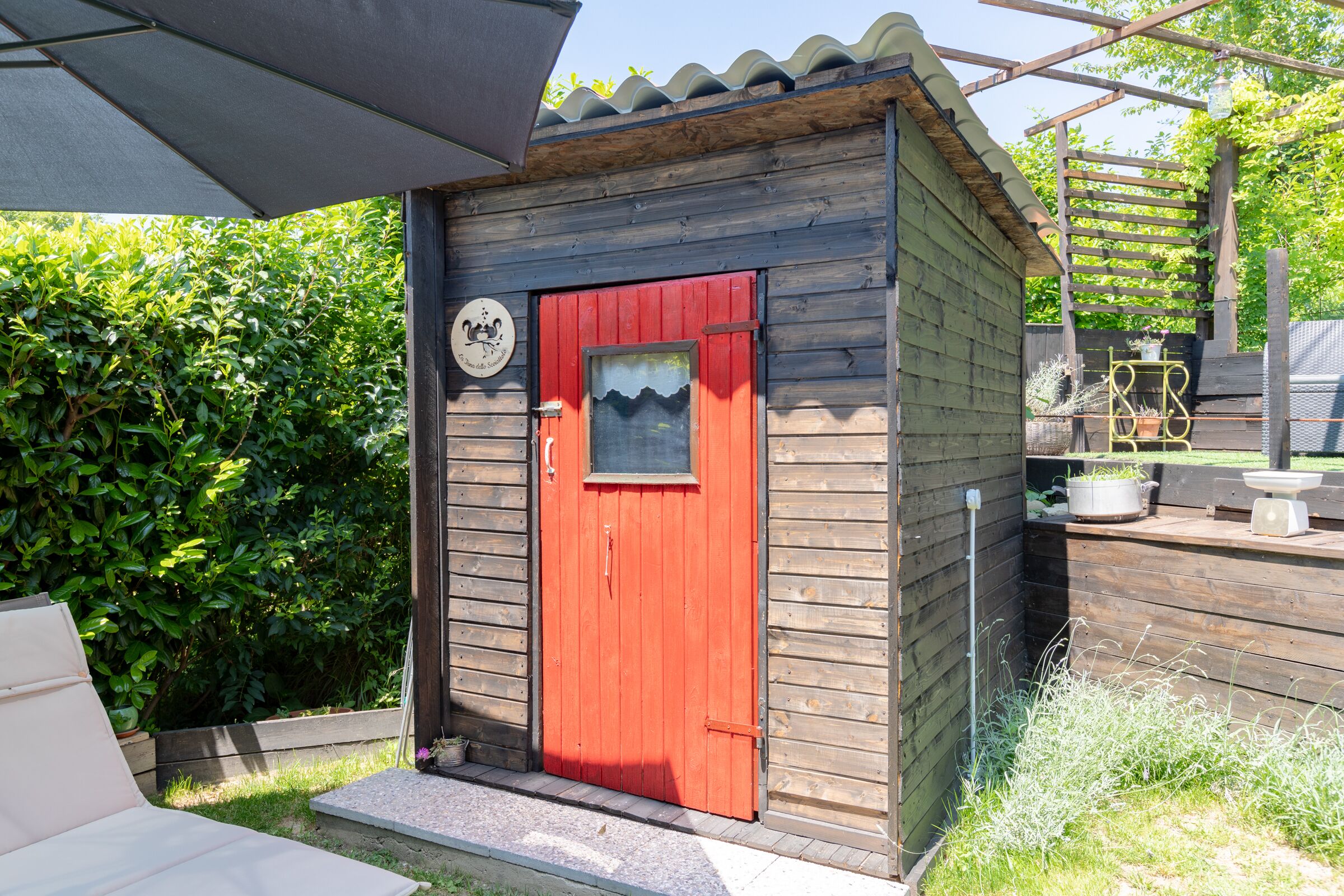 A small wooden structure with a red door, a window, and a sign on the door.