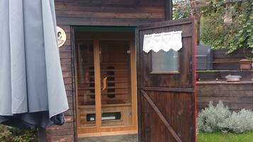 Una cabaña de madera con la puerta abierta, mostrando un cuarto con ventana y una mesita.