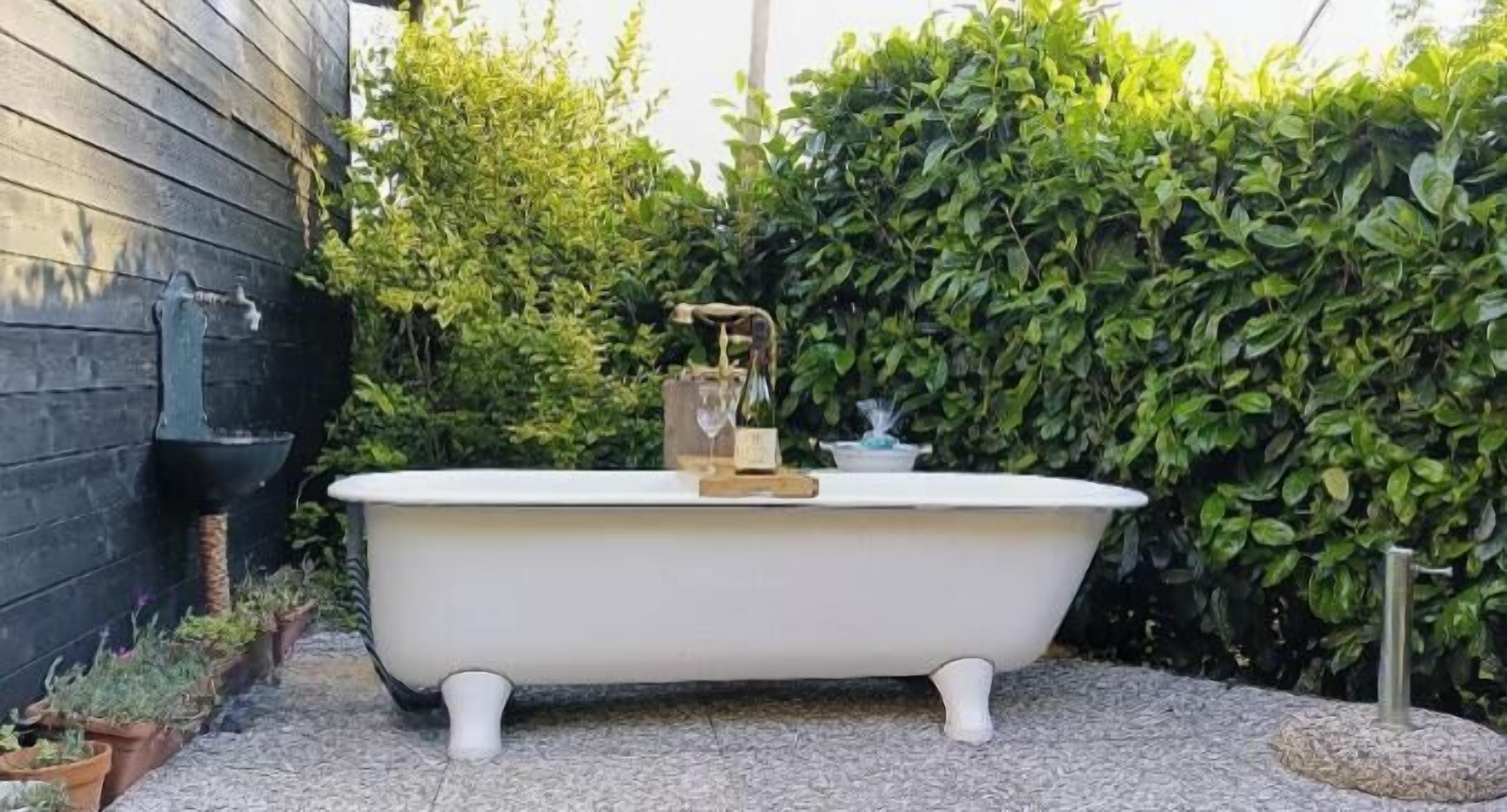 Una vasca da bagno bianca, indipendente, in un giardino con un muro in legno e fitta vegetazione sullo sfondo.