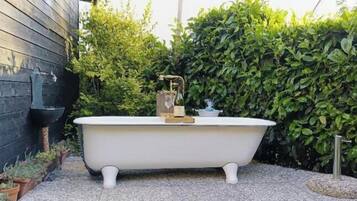Una vasca da bagno bianca, indipendente, in un giardino con un muro in legno e fitta vegetazione sullo sfondo.