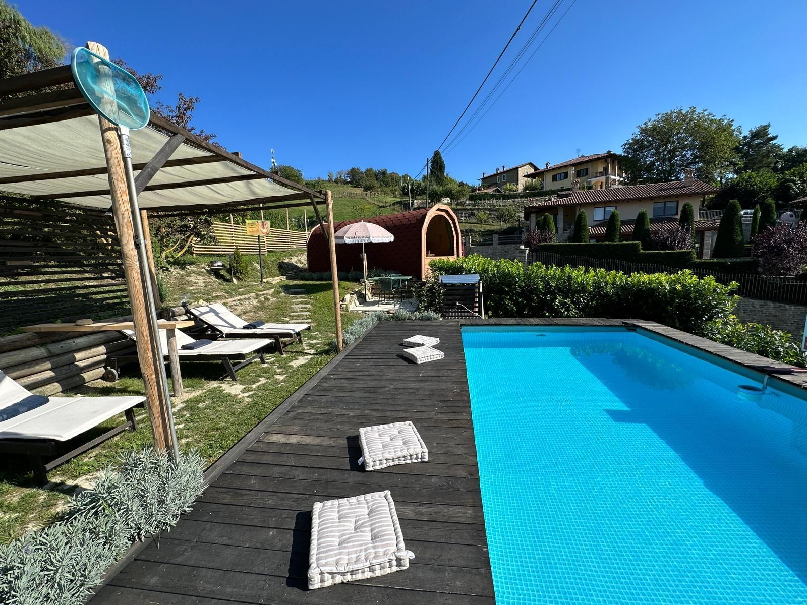 Una piscina con muelle de madera, sillas de descanso y una pérgola.