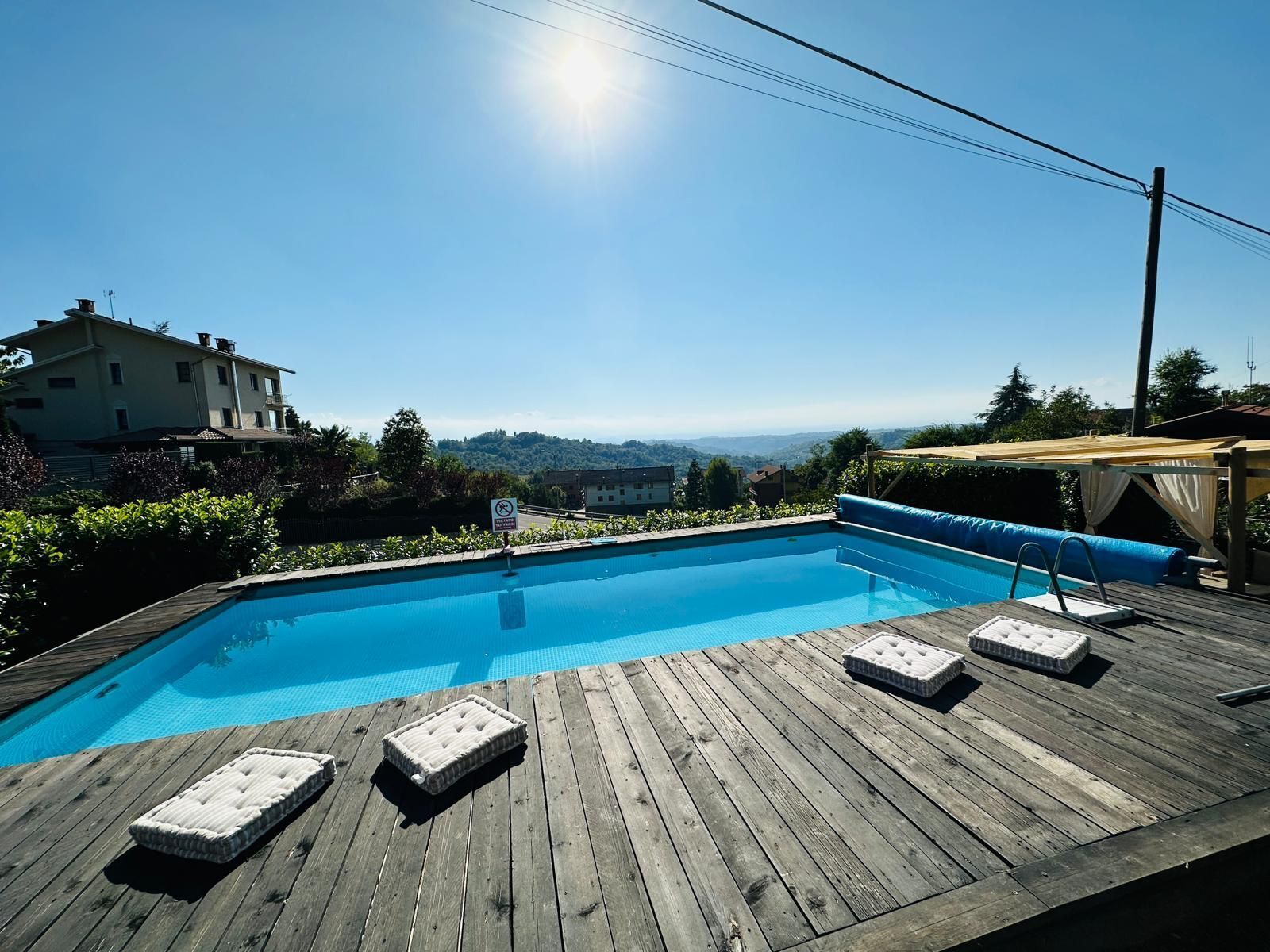 A wooden deck with a swimming pool, lounge chairs, and a view of a hilltop town.