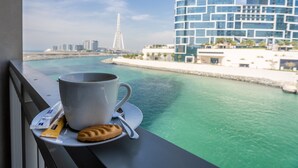 Une tasse de café et un biscuit sur un plateau, près d’une fenêtre donnant sur un plan d’eau, avec des bâtiments en arrière-plan.