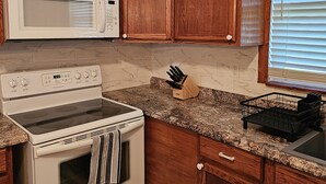 A kitchen with wooden cabinets, a microwave, a stove, and a window with blinds. - Cozy Lakeside Cottage near Legoland, Winter Haven! Florida vacation ready! (Winter Haven)