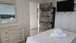 A bedroom with a bed, a dresser, a mirror, and a TV. - Cozy Lakeside Cottage near Legoland, Winter Haven! Florida vacation ready! (Winter Haven)