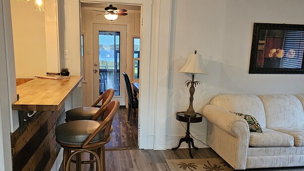 A kitchen with a wooden countertop and bar stools, a dining area with a table and chairs, a sofa, and a floor lamp. - Cozy Lakeside Cottage near Legoland, Winter Haven! Florida vacation ready! (Winter Haven)