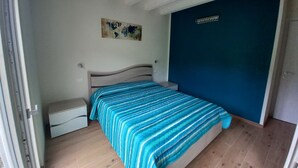 A bedroom with a bed, a nightstand, a wall-mounted shelf, and a blue accent wall. - Casa Maria, Nuovo Appartamento con Vista Lago (Albisano di Torri del Benaco)