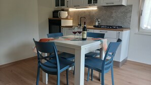 A modern kitchen with white cabinets, a microwave, a kettle, and a dining table with blue chairs. - Casa Maria, Nuovo Appartamento con Vista Lago (Albisano di Torri del Benaco)
