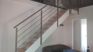 A modern staircase with metal railings and wooden steps, leading to an upper floor. A dining area with a table, chairs, and a bottle of wine is visible. - Casa Maria, Nuovo Appartamento con Vista Lago (Albisano di Torri del Benaco)
