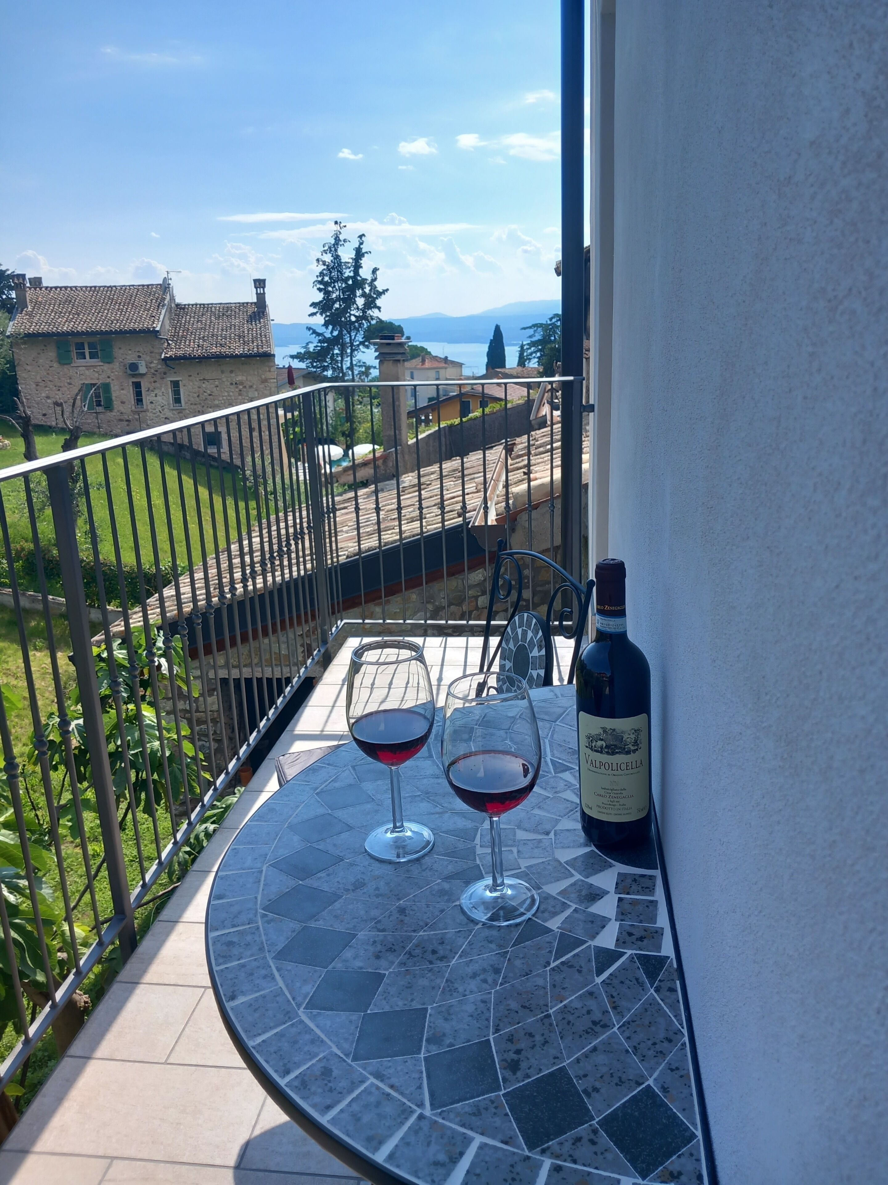 A balcony with two wine glasses and a bottle of wine, overlooking a scenic view of houses and a body of water.