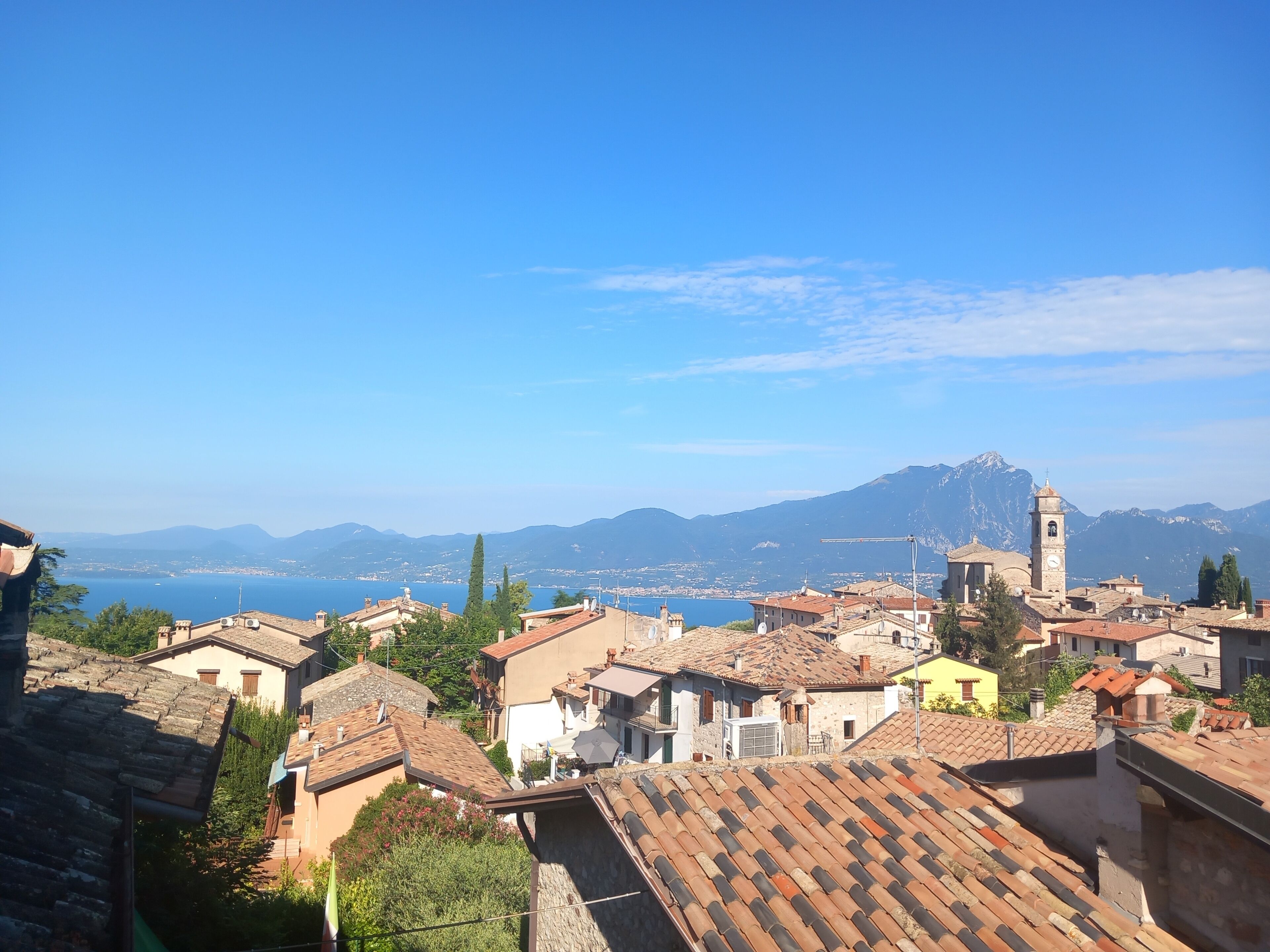 A coastal town with traditional architecture, a prominent clock tower, and a view of the sea and mountains in the background.