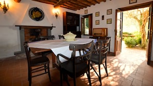 Un comedor con una mesa preparada para cuatro personas, rodeado de sillas, una chimenea y vistas del jardín a través de una puerta abierta.