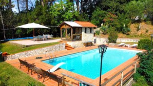 Una piscina con terraza de piedra, rodeada de vegetación y un pequeño pabellón.