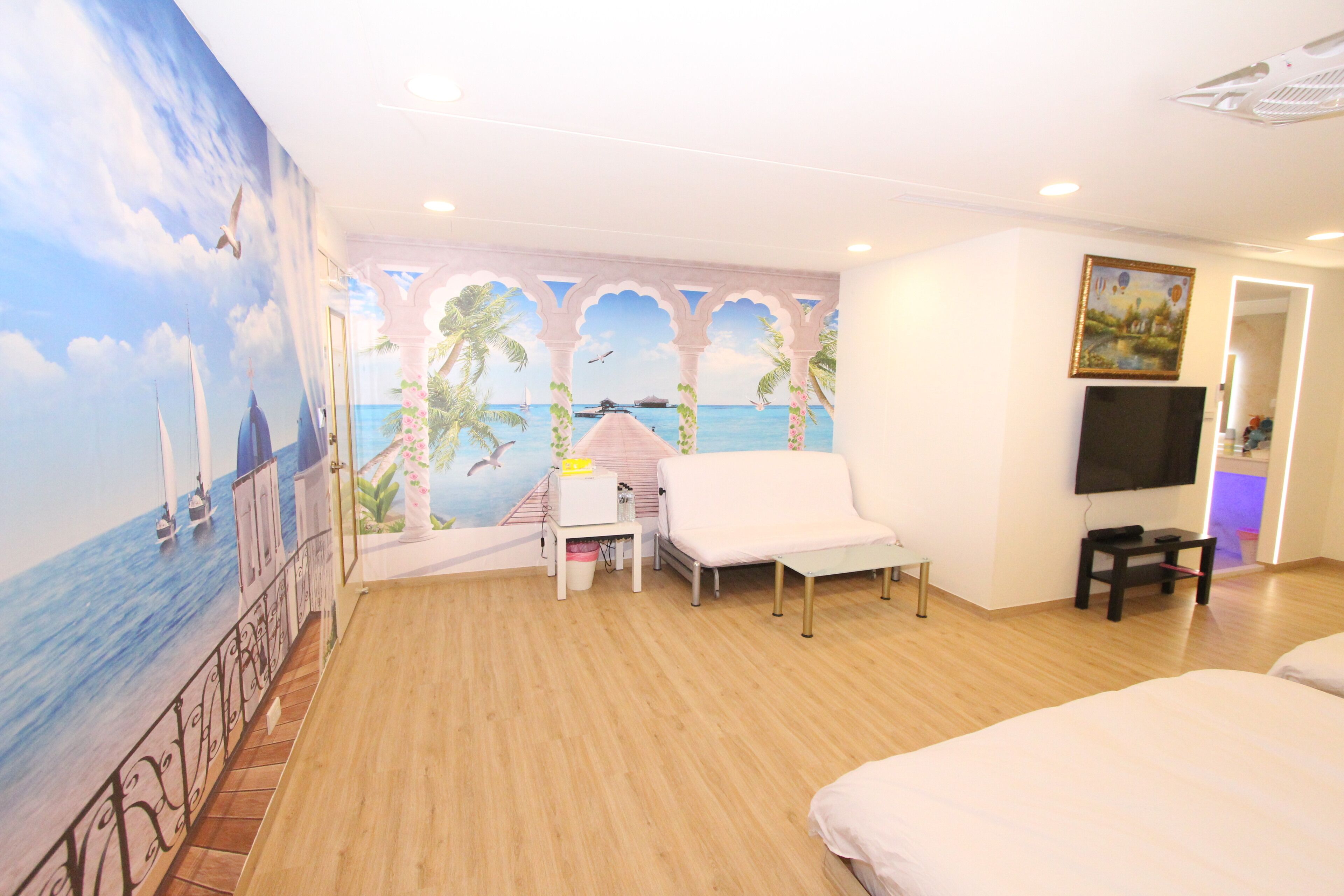 A hotel room with a mural of a beach scene, a white sofa, a small table, and a TV on the wall.