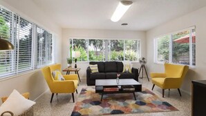 Una sala de estar con un sofá negro, sillones amarillos, una mesa de centro y una alfombra colorida.