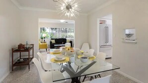 Un comedor moderno con una mesa de vidrio, sillas blancas y una araña.