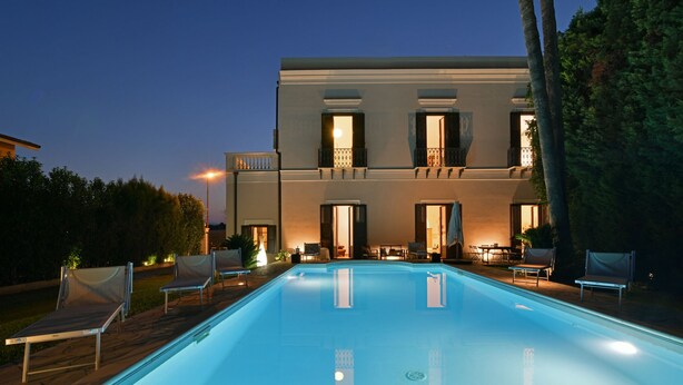 A modern two-story building with a swimming pool, outdoor seating, and a well-lit entrance. - Villa Afrodite 8, Emma Villas (Milazzo)