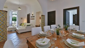 A dining area with a wooden table set for a meal, surrounded by white chairs. - Villa Afrodite 8, Emma Villas (Milazzo)
