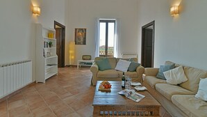 A living room with a beige sofa, a coffee table with a magazine, and a bookshelf. - Villa Afrodite 8, Emma Villas (Milazzo)