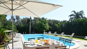 A poolside dining area with a table set for breakfast, surrounded by lounge chairs and an umbrella. - Villa Afrodite 8, Emma Villas (Milazzo)
