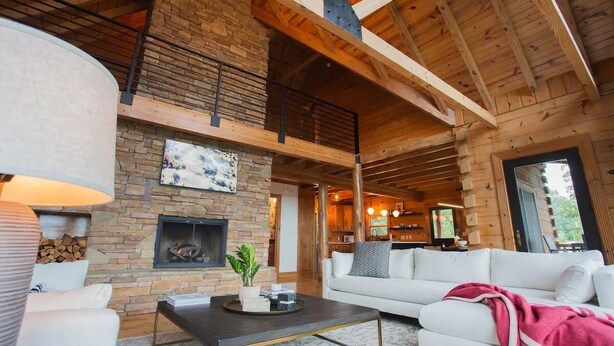 A spacious living area with a stone fireplace, wooden beams, a white sofa, and a coffee table. - The Ridge: A Modern Cabin (Bostic)