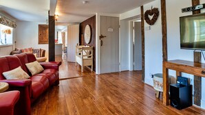 Un vaste espace de vie agrémenté d’un canapé en cuir rouge, d’un plancher en bois, d’un téléviseur fixé sur un meuble en bois et d’une cheminée.