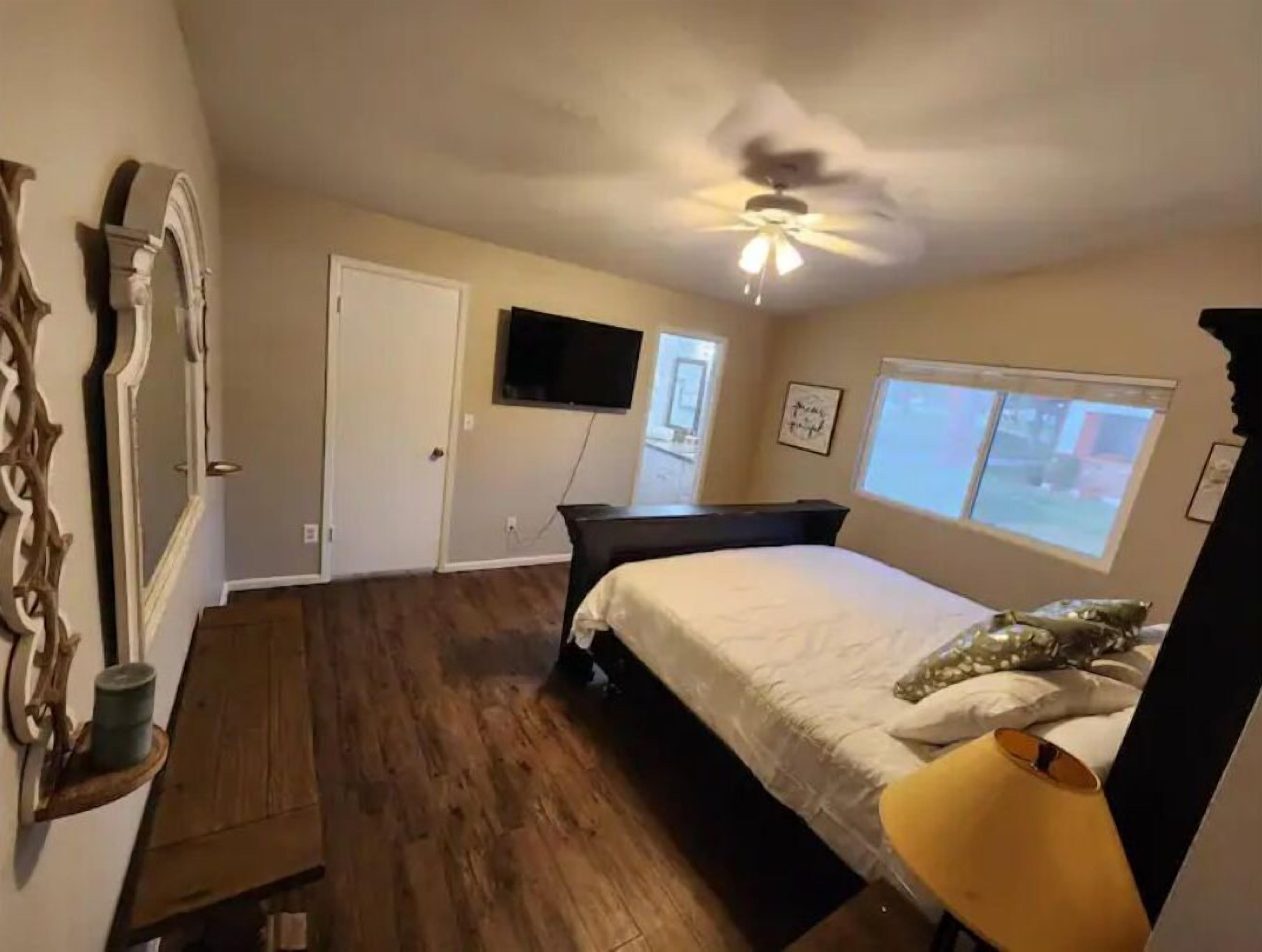 Ein Schlafzimmer mit einem Bett, einem Deckenventilator, einem Fernseher und einem Fenster.