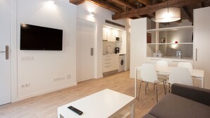A modern living room with a flat-screen TV, a sofa, a dining table, and a kitchen in the background. - Alissia 1 - Habitat Apartments (Barcelona)