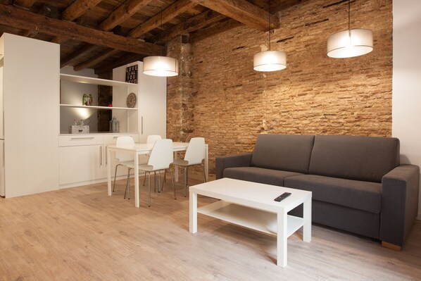 A modern kitchen with white cabinetry, a dining area with white chairs, a gray sofa, and a white coffee table.