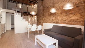 A modern interior with a wooden staircase, a gray sofa, a white table, and pendant lighting.