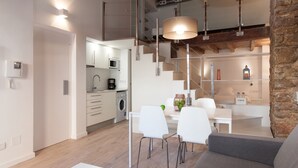 A modern kitchen with a microwave, coffee maker, and a dining area with white chairs and a table.