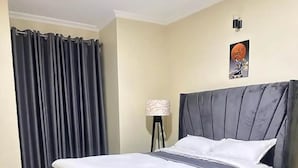 Una cama bien hecha con un cabecero gris, una alfombra estampada y una lámpara sobre un soporte.