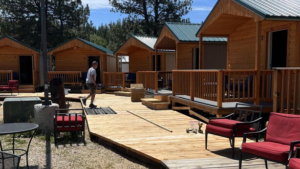 A wooden deck with outdoor seating, surrounded by cabins with green roofs. - The Gold Mine Hotel (Idaho City)