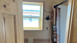 A wooden interior with a window, a shelf with various items, and a door. - The Gold Mine Hotel (Idaho City)
